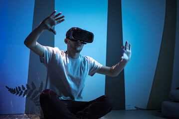 Young man wearing VR glasses sitting in a yoga pose on the virtual reality escape room floor. Fun, entertainment, and innovation concepts.