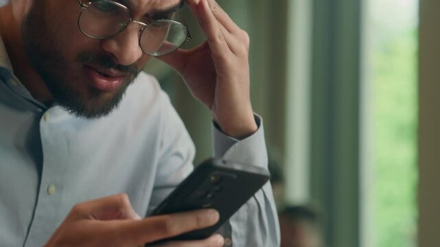 Shocked male Arabian Indian business man hold cellphone read bad news shock stress confused mobile phone notification message sad anxious frustrated guy businessman with smartphone in cafe restaurant