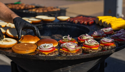 Cooking appetizing burgers. The buns are perfectly toasted. The sizzling burger patties are grilled outdoors. Burgers are assembled with fresh toppings.