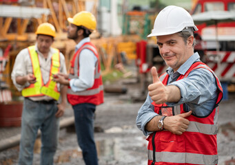 Thump up Mature caucasian engineer man worker with team and spare crane background	
