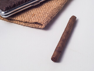 Mini cigar with storage case made of leather, lying on burlap fabric on white background