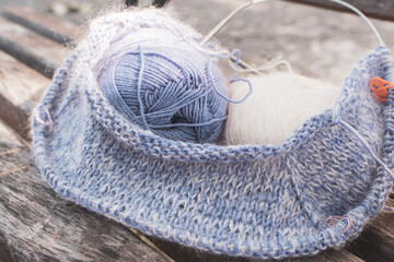 Blue and white wool yarn ball with knitting needles and marker. Blue wool and white mohair with beautiful knitting pattern. Knitting hobby. Knitwear concept. Needlework on wooden bench.