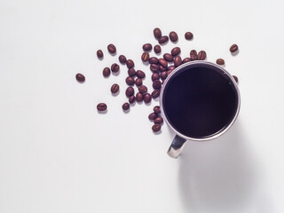 Brewed coffee in a stainless steel mug, with coffee beans on a white background