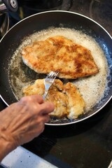 Close-up of an elderly woman's hand frying cutlets in a pan