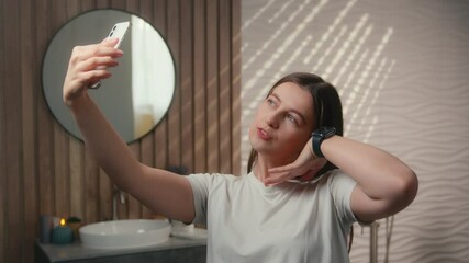 Caucasian woman beauty blogger vlogger model influencer selfie photo mobile phone social media skincare blog vlog in home bathroom carefree happy female girl posing face grimace laugh hold cellphone