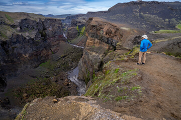 Fototapeta premium A hiker looking into a deep gorge with a river running at the bottom and steep rock walls on either side the Markarfijor canyon, Botnar hut, Laugavegur trail, Iceland