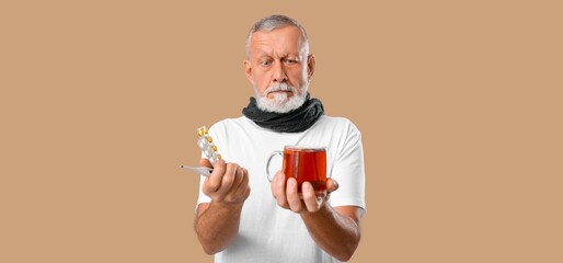 Ill old man with pills, thermometer and hot tea on beige background