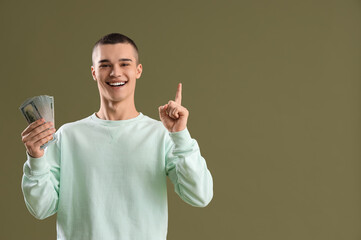 Young man with dollar banknotes pointing at something on green background