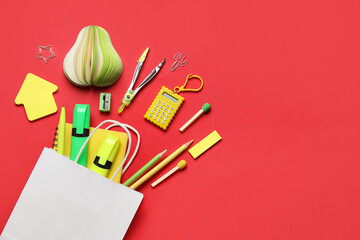 Composition with paper bag and different stationery on red background