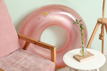 Chair, stool with vase and inflatable ring near pale green wall in room
