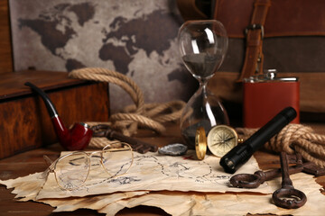 Treasure map with travel equipment, hip flask and smoking pipe on brown wooden background