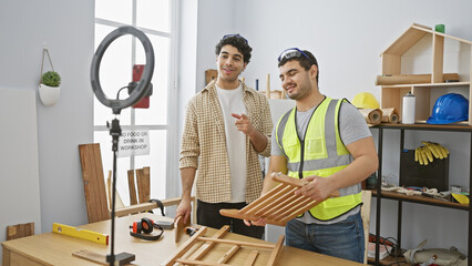 Two men collaborating in a brightly lit carpentry workshop, one holding wooden chair parts and the other gesturing positively.