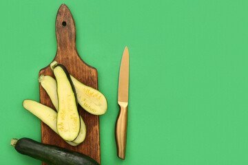 Wooden board with slices of fresh zucchini on green background
