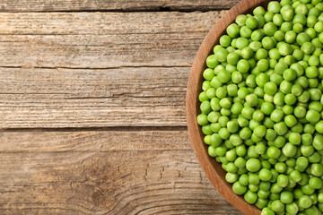 Fresh green peas in bowl on wooden table, top view. Space for text