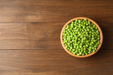 Fresh green peas in bowl on wooden table, top view. Space for text