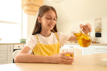 Little girl pouring apple juice into glass in kitchen