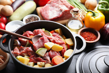 Cooking stew. Uncooked meat, vegetables and pot on black table