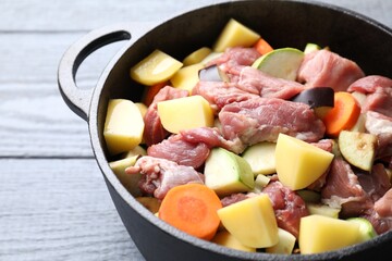 Cooking stew. Uncooked meat and vegetables in pot on light grey wooden table, closeup