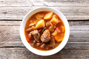 Delicious stew with vegetables in bowl on wooden table, top view