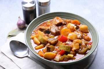 Delicious stew with vegetables in bowl, spices and spoon on table, closeup