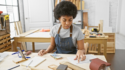 African american woman working thoughtfully in her carpentry studio with various woodworking tools...