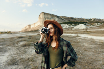 Fashionable woman in plaid shirt and hat capturing memories with vintage camera on a sunny day