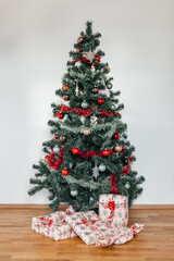 Christmas tree with presents under it on the wooden floor and white wall background