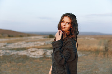 Serene young woman in cozy sweater standing under the golden sunset in vast field