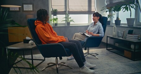 African American teen sits and talks with psychotherapist. Boy discusses psychological trauma, finds solutions during therapy session. Psychological assistance. Psychology and mental health concept.