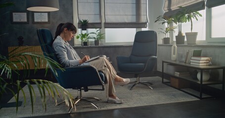 Female therapist sits in chair, takes notes in notebook. African American teen boy comes in psychological office on counseling session. Professional psychologist starts therapy, talks to teenager.