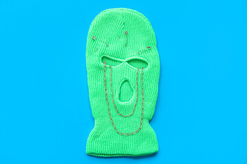 Balaclava with stylish necklace and safety pins on color background