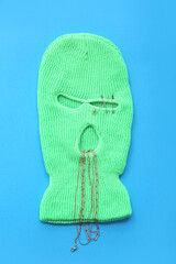 Balaclava with necklaces and safety pins on color background