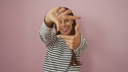 Fototapeta premium Smiling young hispanic woman making framing gesture with hands against a pink isolated background, portraying creativity and positivity.