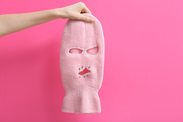 Woman holding balaclava with safety pins on pink background, closeup