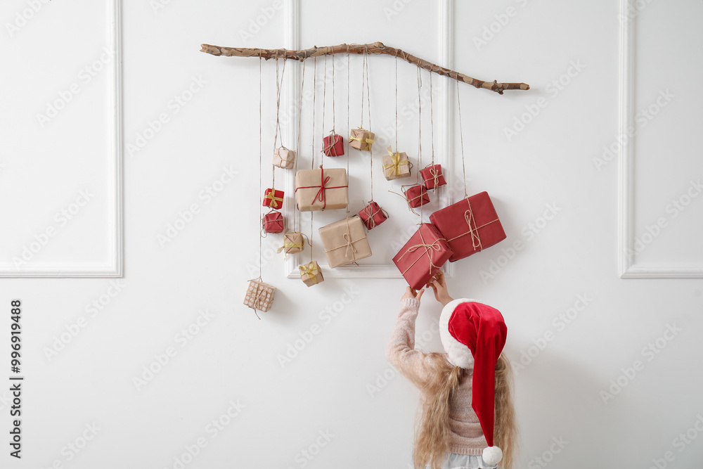 Canvas Prints Cute little girl in Santa hat and Christmas advent calendar hanging on light wall