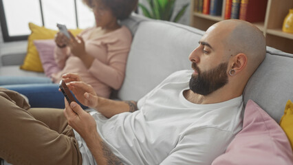 Fototapeta premium Interracial couple lounging on a couch with their smartphones in a modern living room at home.