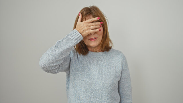 A mature woman covers her eyes with her hand against a white isolated background, evoking concepts of avoidance or surprise
