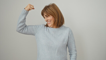 Joyful middle-aged woman flexing arm muscles against isolated white background, showing strength...