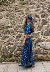 Unrecognisable young woman dressed in a blue outfit looking at an old stone wall