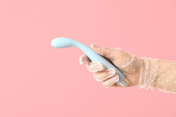 Female hand in laced glove with vibrator on pink background, closeup