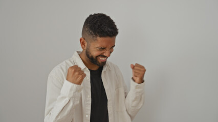 A young black man in a white shirt celebrates with clenched fists against a white background