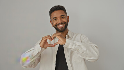 A smiling young african american man making a heart shape with his hands, isolated over a white...
