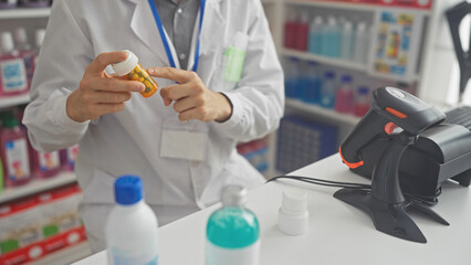 A young man working in a pharmacy examines a bottle of medication against the backdrop of shelves stocked with products.