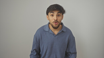 Young, surprised arab man with a beard, wearing a blue shirt, posing against an isolated white background.