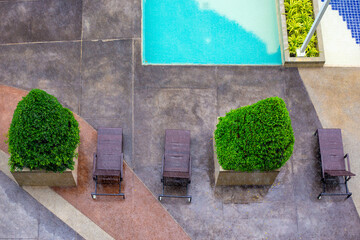 Sun loungers and decorative green plants in the recreation area near the pool on a rainy day, view...