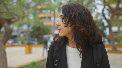 A thoughtful woman in a park with blurred cityscape background, portraying a serene urban outdoor moment.