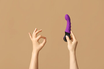 Woman holding vibrator and showing OK gesture on color background, closeup