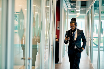 Businessman, walking and phone in office for music, communication and networking with earphones. Lawyer, mobile and listening to online press release, legal podcast and research with client recording