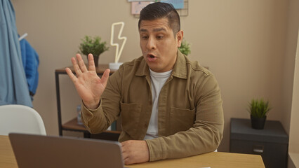 Handsome hispanic man gesturing during a video call in a modern home office setting.