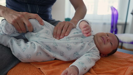 Orthopedist adjusting newborn’s body on an orange towel to relieve body pains, as the baby yawns and falls asleep